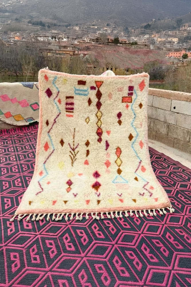 Tapis berbère avec des motifs géométriques colorés en rose, jaune et bleu sur un fond crème.