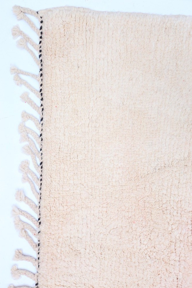 Tapis berbère en laine beige, avec des franges et un design minimaliste, ajoutant une touche de chaleur à votre intérieur.