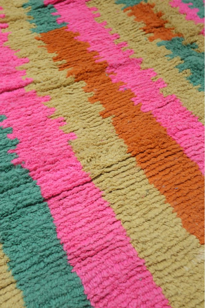 Tapis berbère coloré avec des motifs géométriques en rose, orange, vert et beige, parfait pour une ambiance chaleureuse.