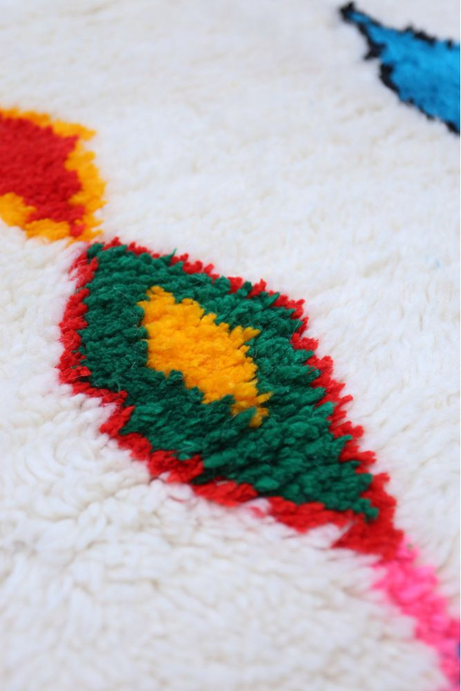 Tapis berbère aux motifs géométriques colorés avec des tons de rouge, vert, jaune et bleu sur fond crème.