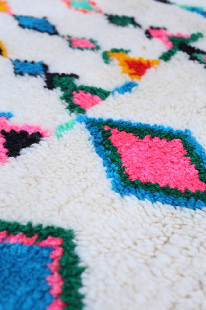 Tapis berbère aux motifs géométriques colorés, dominé par le crème, le rose, le bleu et le vert vif.