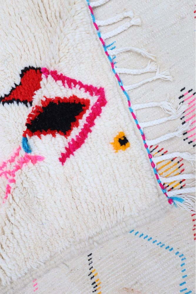 Tapis berbère en laine avec motifs géométriques colorés, dominé par le blanc, le rouge et le rose.