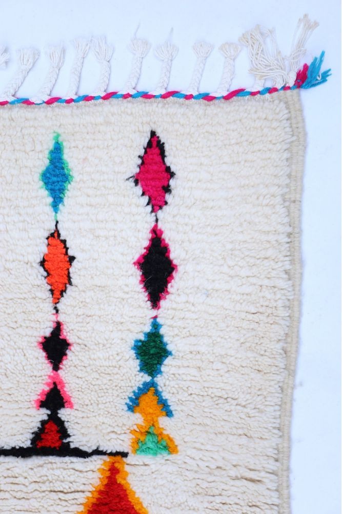 Tapis berbère aux motifs géométriques colorés avec des teintes beige, noir, rose, orange et vert.