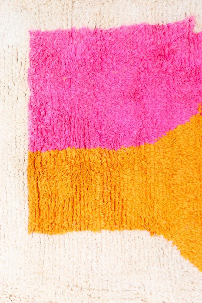 Tapis berbère moderne avec des couleurs vives rose et orange sur un fond crème, motifs géométriques audacieux.