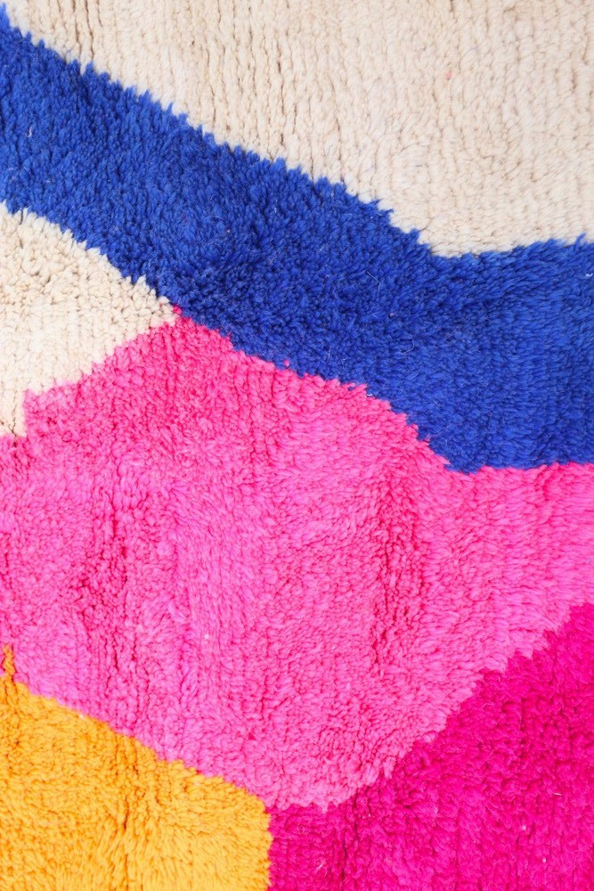 Tapis berbère coloré avec des motifs géométriques en bleu, rose et jaune sur fond crème.
