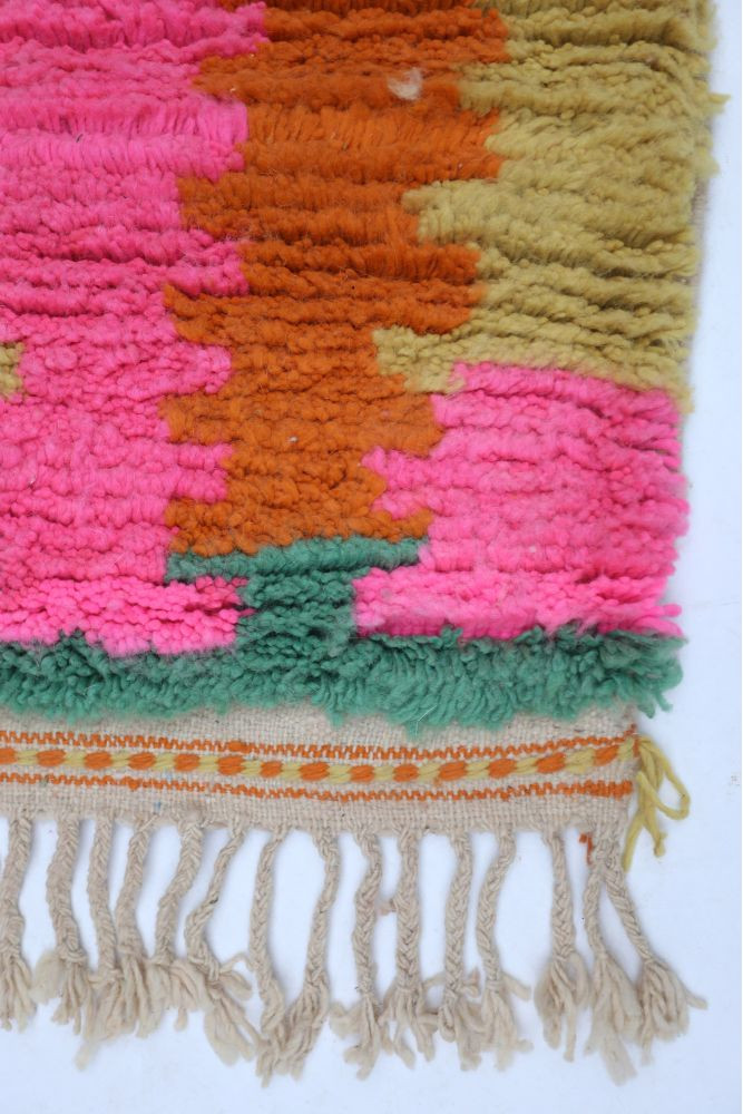 Tapis berbère coloré avec des motifs géométriques en rose, orange, vert et beige, parfait pour une ambiance chaleureuse.