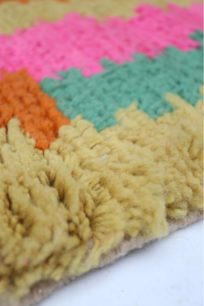 Tapis berbère coloré avec un motif géométrique, dominant en rose, vert, orange et jaune.