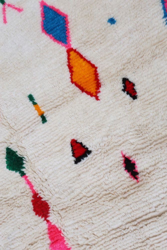 Tapis berbère aux motifs colorés, dominant les teintes crème, rouge, bleu et orange avec des formes géométriques.