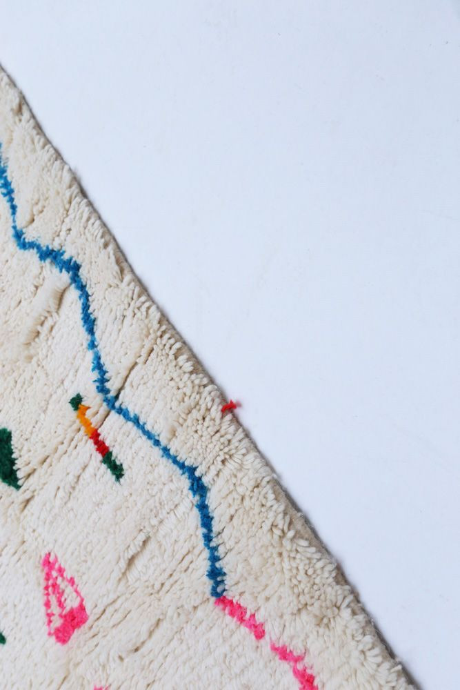 Tapis berbère en laine, style contemporain avec des motifs colorés en rose, bleu et vert sur fond crème.