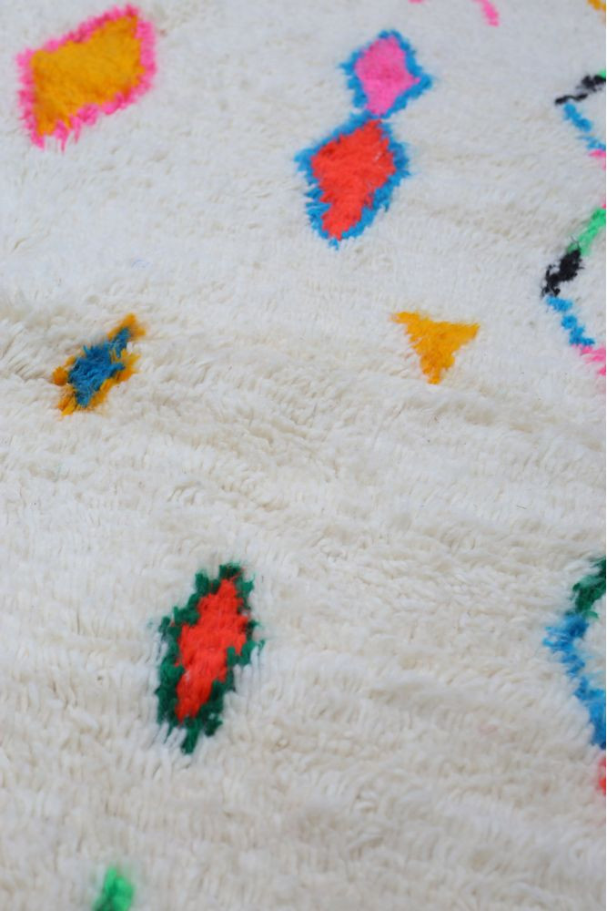 Tapis berbère en laine avec motifs géométriques colorés sur fond blanc, incluant des teintes vives de rose, bleu, orange et vert