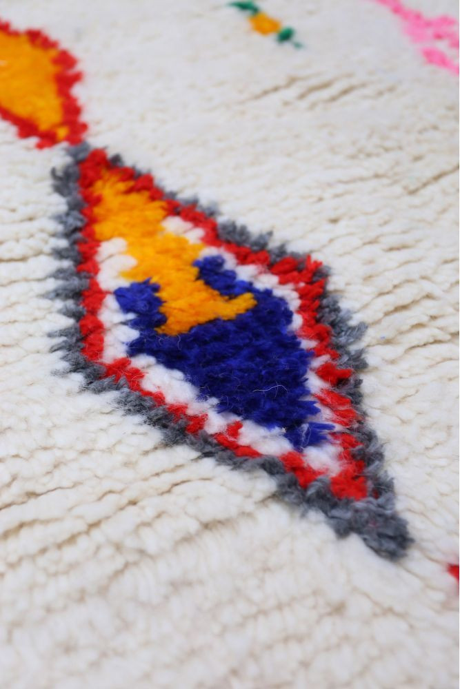 Tapis berbère aux motifs géométriques colorés avec des nuances de bleu, orange, rouge et blanc sur fond crème.