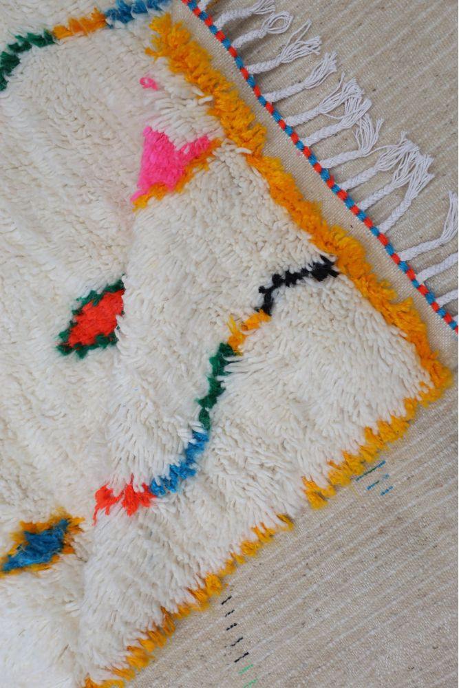 Tapis berbère aux couleurs vives, motifs floraux en rose, orange, bleu et noir sur fond crème, idéal pour un intérieur chaleureu