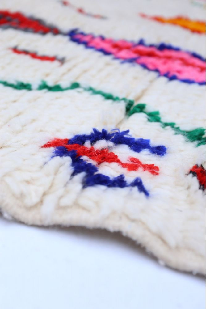 Tapis berbère au style traditionnel, avec des motifs colorés en rouge, bleu, vert et rose sur un fond crème.