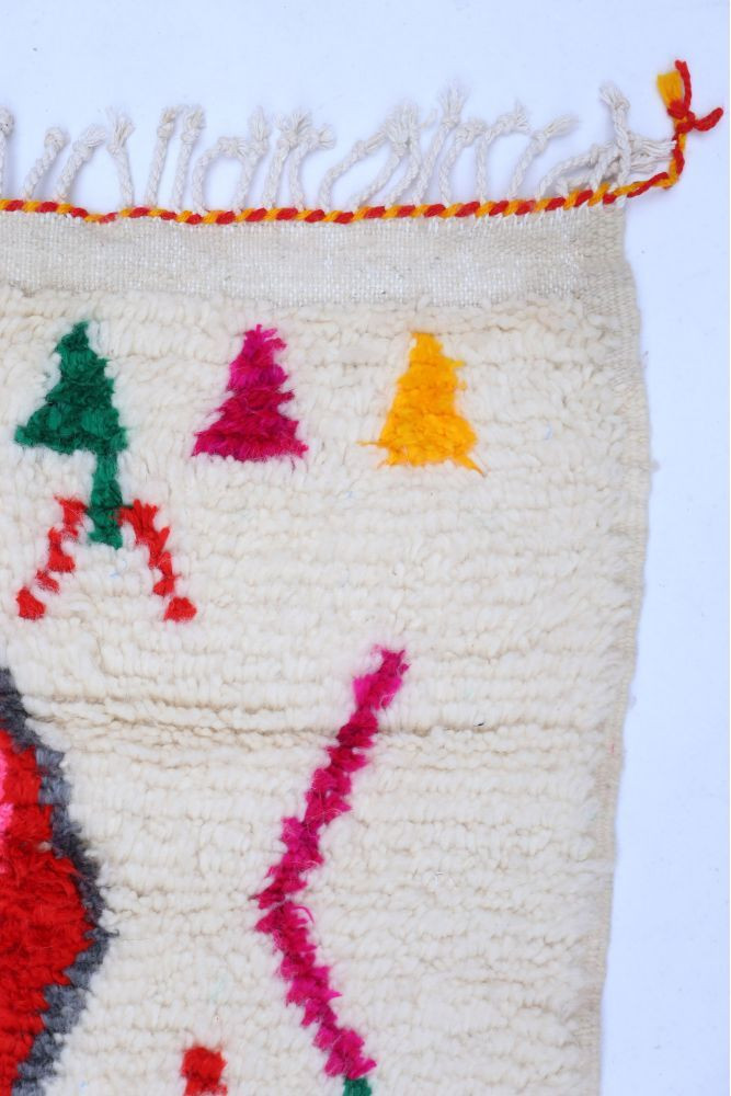 Tapis berbère aux motifs géométriques colorés en rouge, vert, rose et jaune sur fond crémeux.