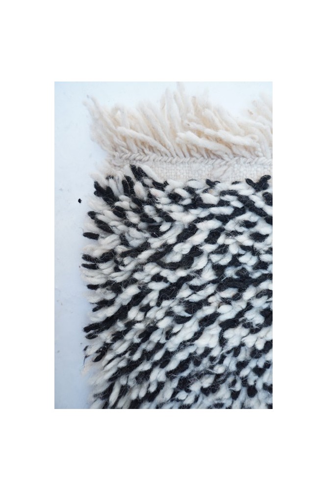 Tapis berbère noir et blanc avec motifs géométriques, texture douce et franges, idéal pour un intérieur élégant.