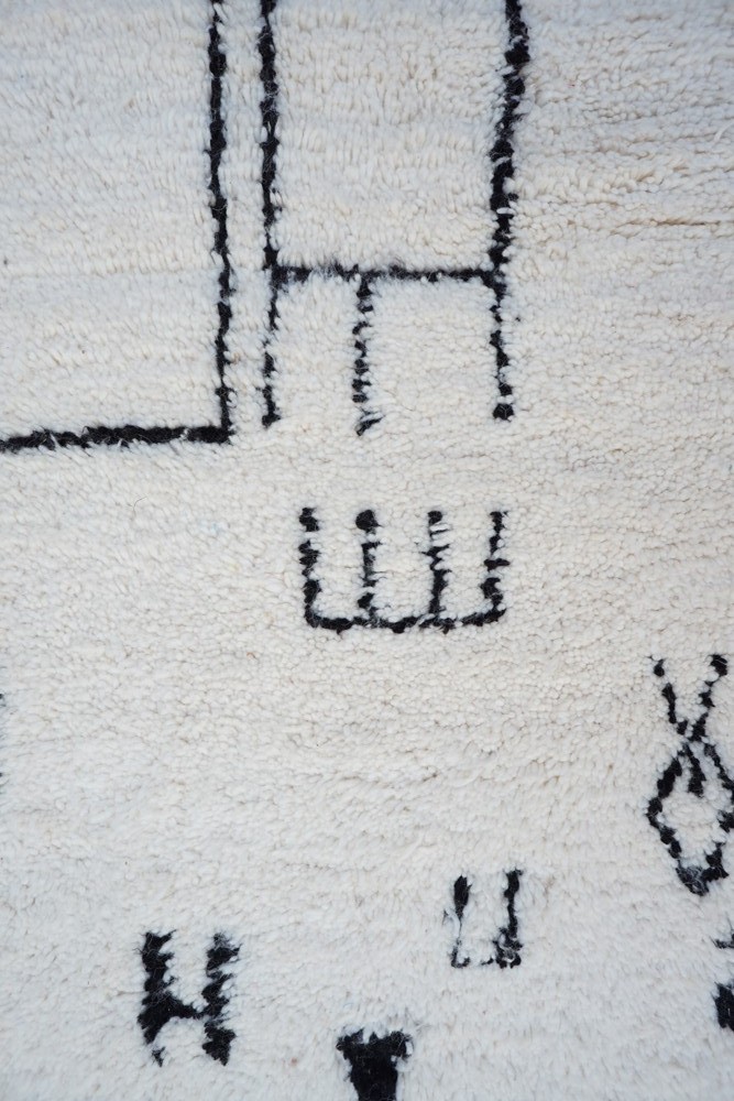 Tapis berbère en laine blanche avec motifs noirs géométriques, ajoutant une touche bohème à votre décoration intérieure.