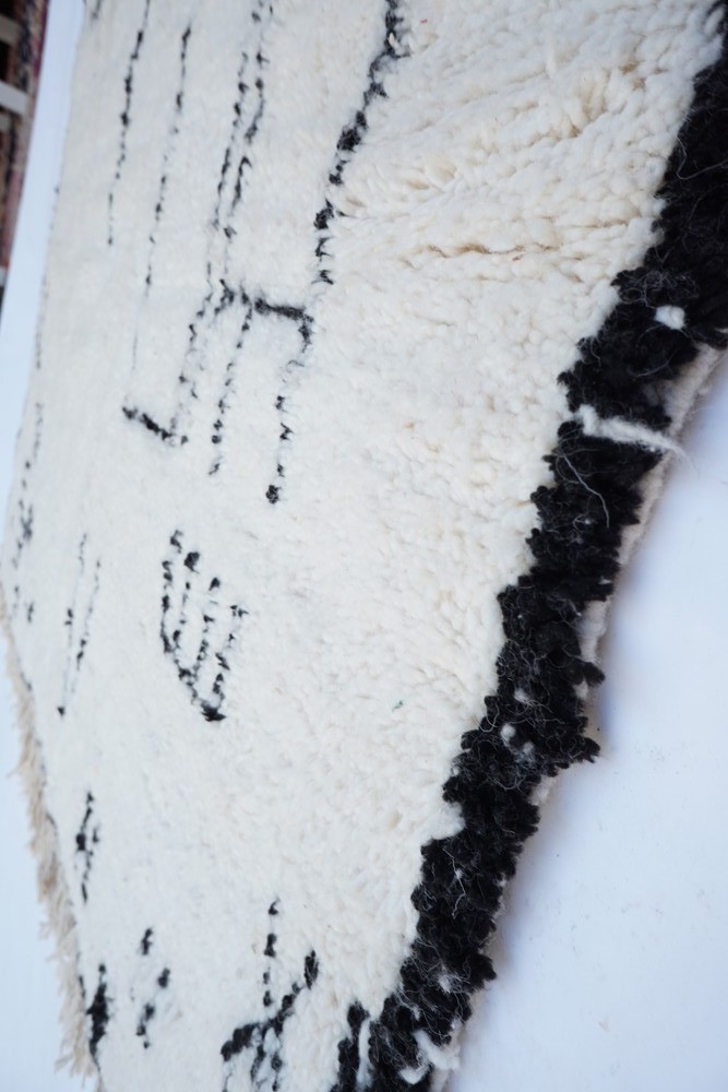Tapis berbère en laine, aux motifs géométriques noirs sur fond crème, ajoutant une touche artisanale à votre intérieur.
