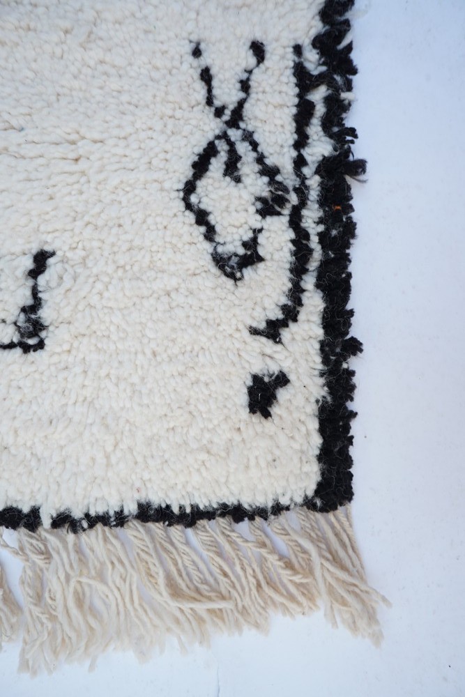 Tapis berbère en laine avec motifs géométriques noirs sur fond crème, bordure frangée pour une touche artisanale.